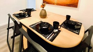Un coin repas avec une table en bois, des chaises noires et un tableau représentant un coucher de soleil sur l’eau.