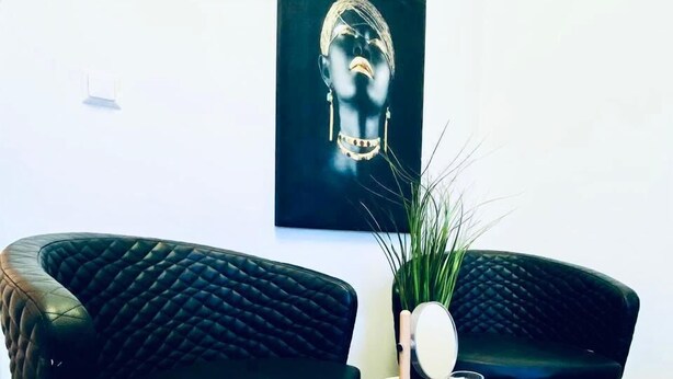 Une pièce comprenant deux fauteuils en cuir noir, une table ronde en métal avec un miroir et une bougie, et une œuvre d’art encadrée accrochée au mur.