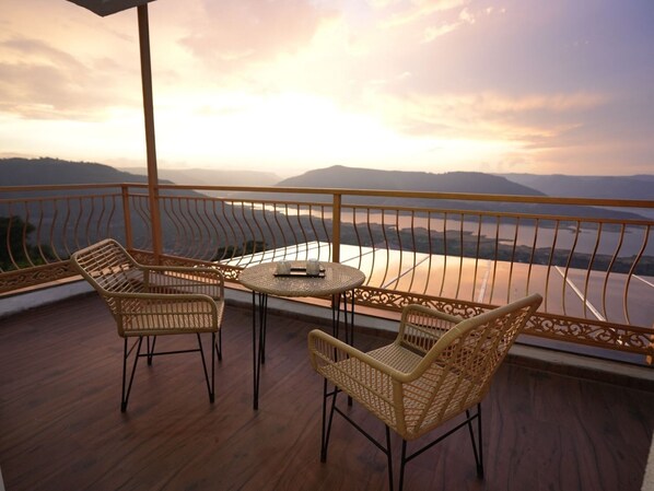 Un balcón con mobiliario de mimbre y una mesa, con vistas a un paisaje montañoso y un río.