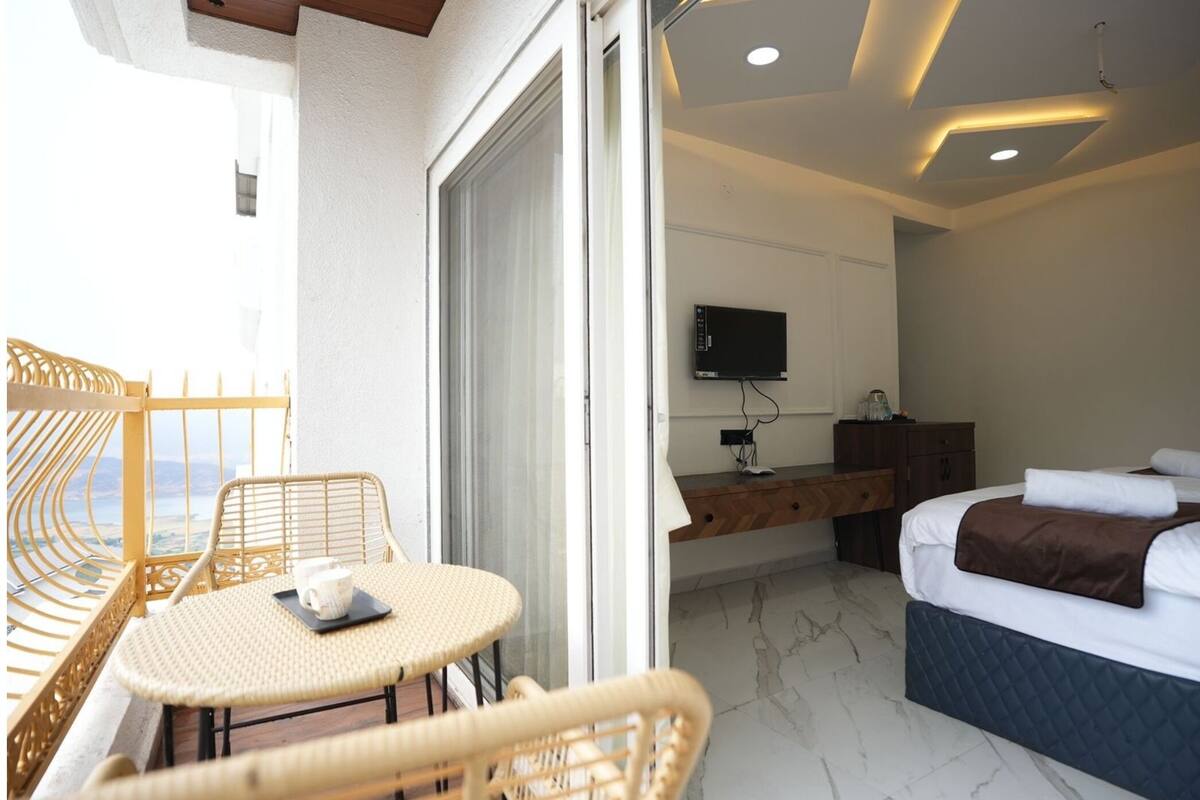 Un balcone con mobili in vimini, un letto con testiera imbottita, una TV montata a parete e una scrivania con un computer.