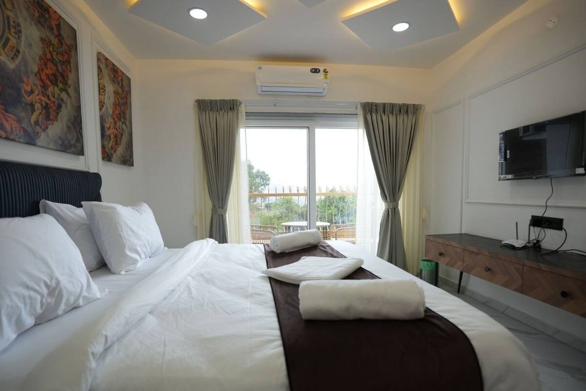 Una camera d'albergo con un letto grande, una scrivania, una TV e un balcone con vista.