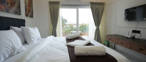 A hotel room with a large bed, a desk, a TV, and a balcony with a view.