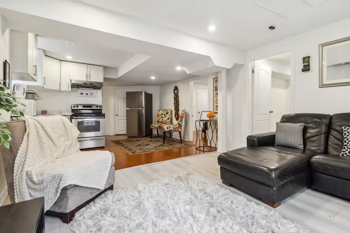 A modern living room with a sofa, a coffee table, and a fireplace. There is a kitchen area with appliances and a dining table.
