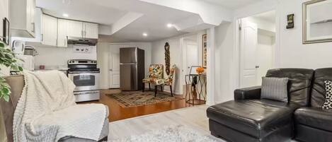 A modern living room with a sofa, a coffee table, and a fireplace. There is a kitchen area with appliances and a dining table.
