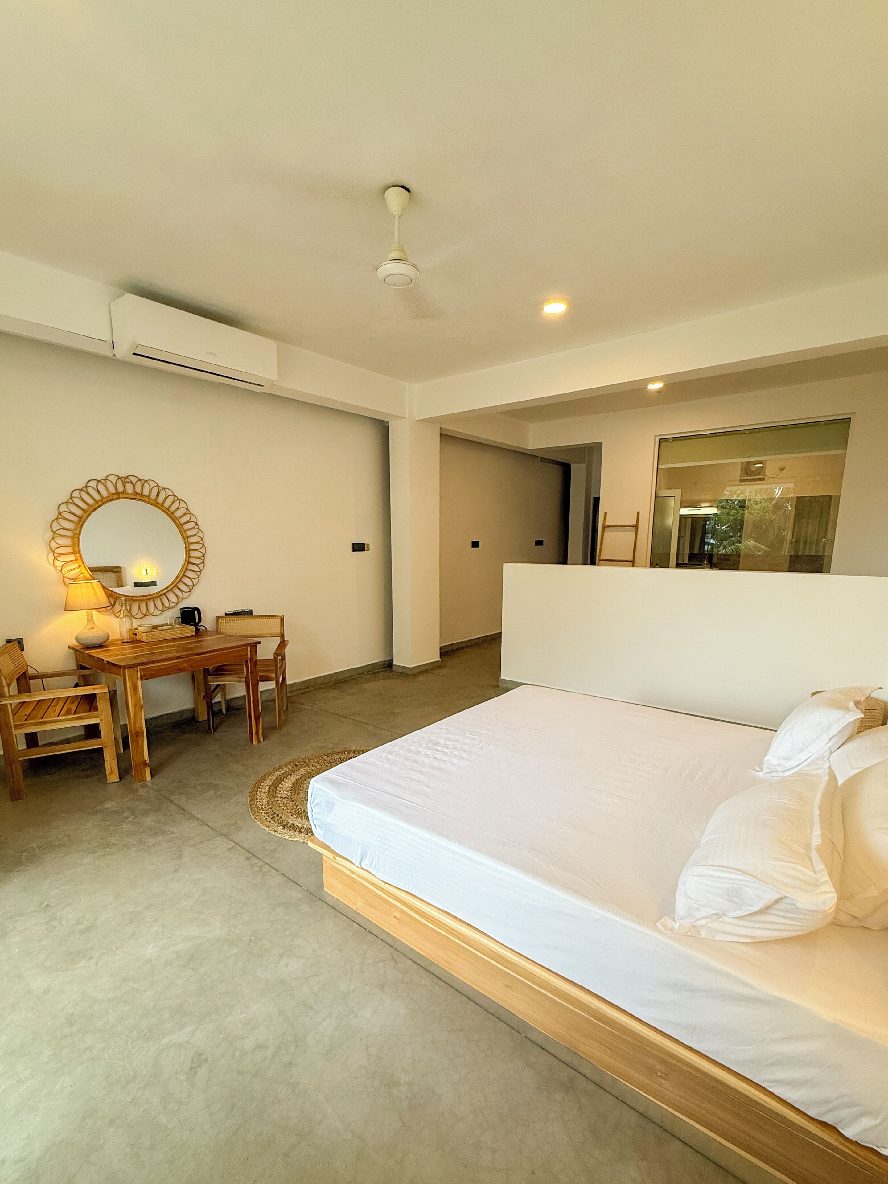 Habitación de hotel con una cama grande, un escritorio de madera con una silla, un espejo redondo y un ventilador de techo.