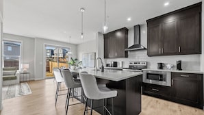 Una cocina moderna con armarios oscuros, una isla grande con taburetes de bar y vista a una zona residencial.