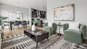 Una sala de estar moderna con una mesa baja oscura, sillones verdes y un cuadro abstracto de gran tamaño.