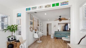 A modern living room with a wooden floor, a blue sofa, a dining area with a white table and chairs, and a ceiling fan. - Coastal Comfort 2BR Getaway St Pete (St. Petersburg)
