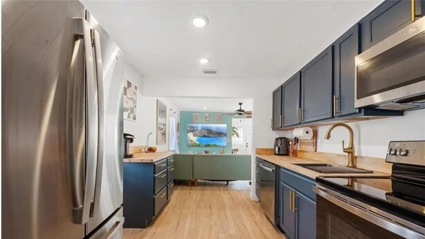 A modern kitchen with stainless steel appliances, dark blue cabinets, and a wooden floor. - Coastal Comfort 2BR Getaway St Pete (St. Petersburg)