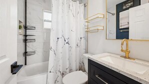 A modern bathroom with a marble shower, a white toilet, a gold faucet, and black cabinets. - Coastal Comfort 2BR Getaway St Pete (St. Petersburg)