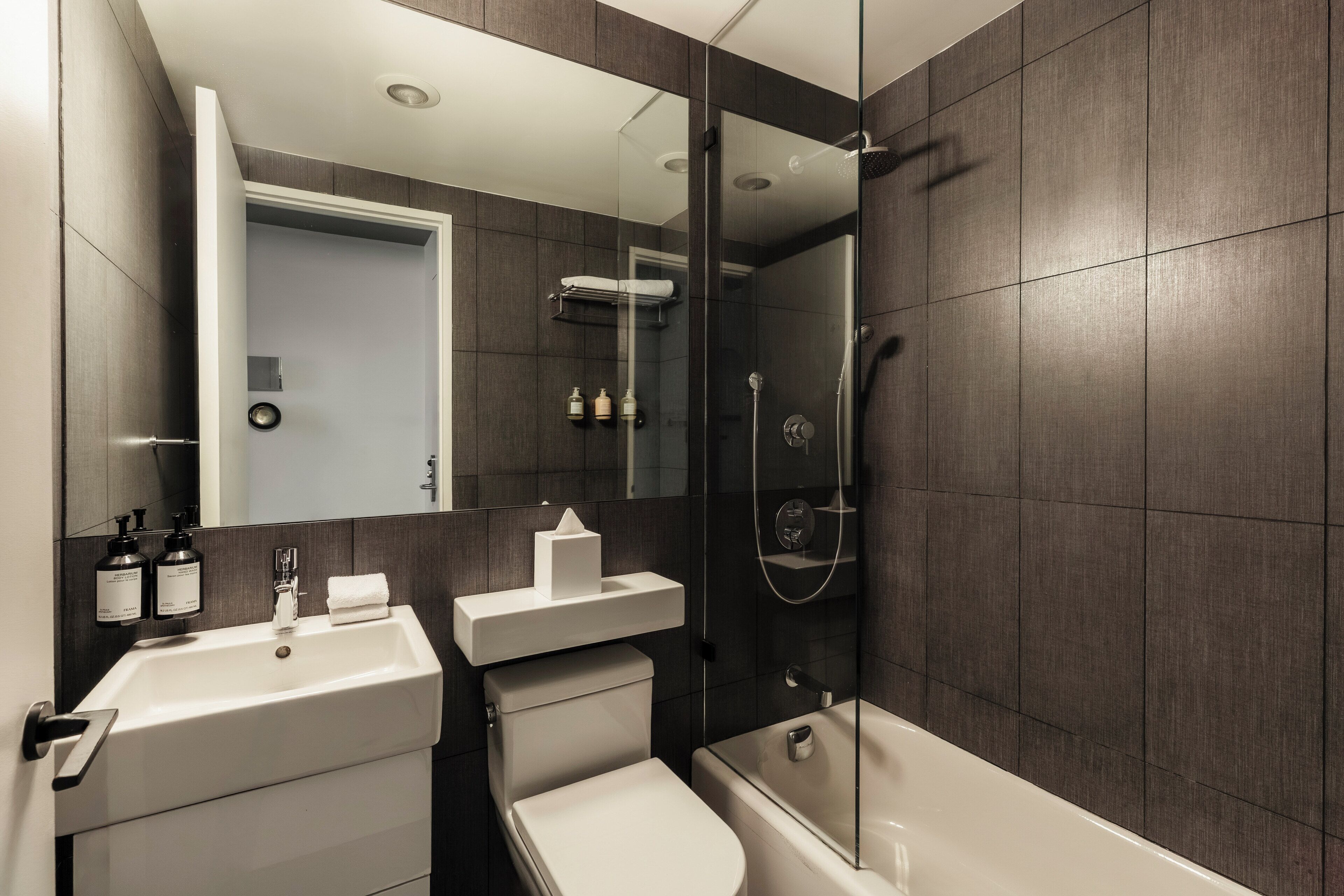 Un baño moderno con ducha envuelta en vidrio, lavamanos blanco y un inodoro.