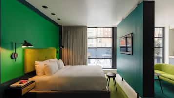 A modern hotel room with a large bed, a green accent wall, a view of the city, and a green sofa.