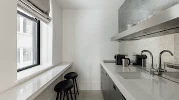 A modern kitchen with a white countertop, stainless steel appliances, and a window with blinds.