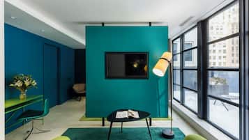Quarto moderno com paredes verde-água, televisão com moldura preta, sofá verde e uma grande janela com vista para a cidade.