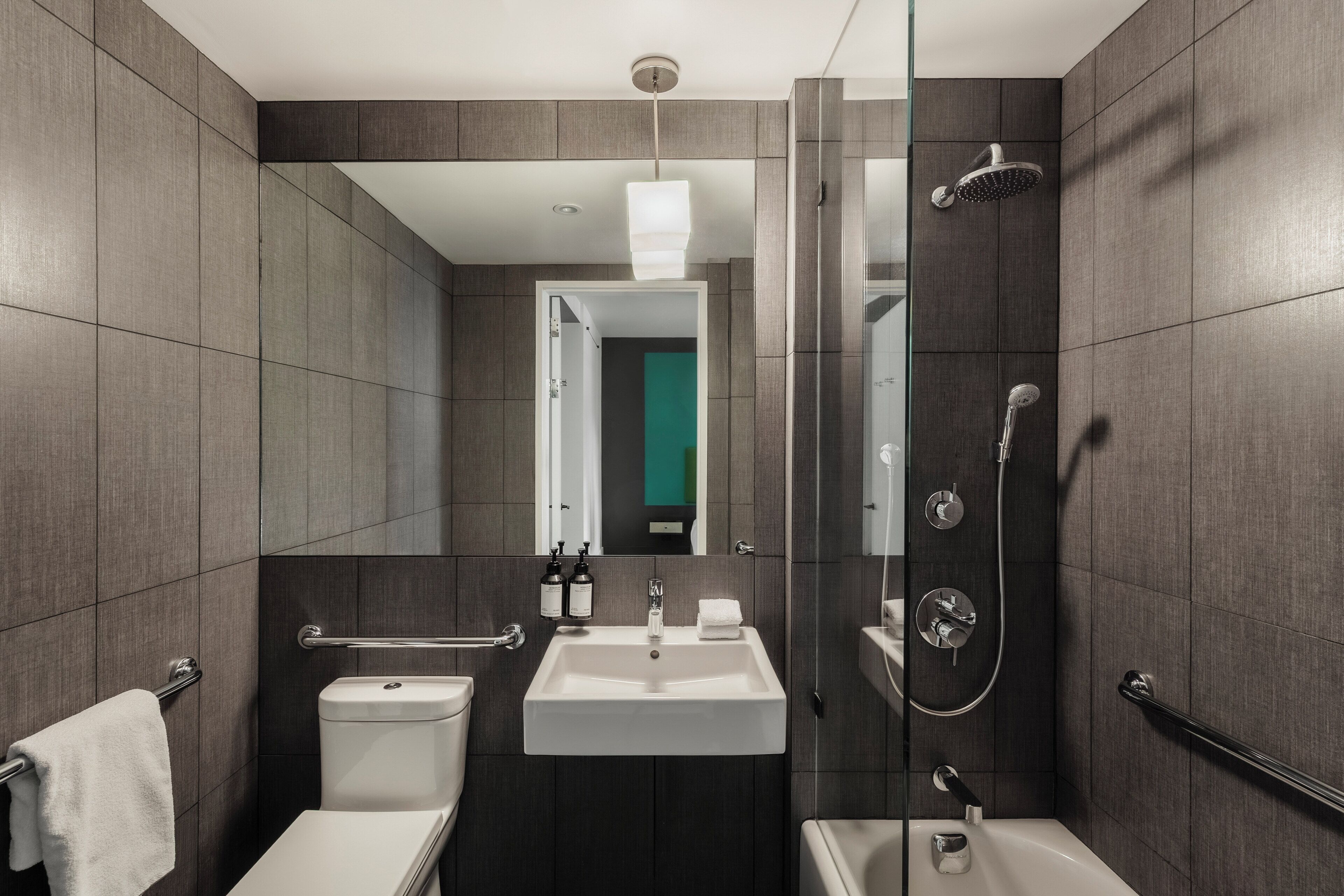 A modern bathroom with a shower, toilet, and sink, featuring a glass partition and a mirror.
