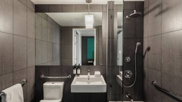 A modern bathroom with a shower, toilet, and sink, featuring a glass partition and a mirror.