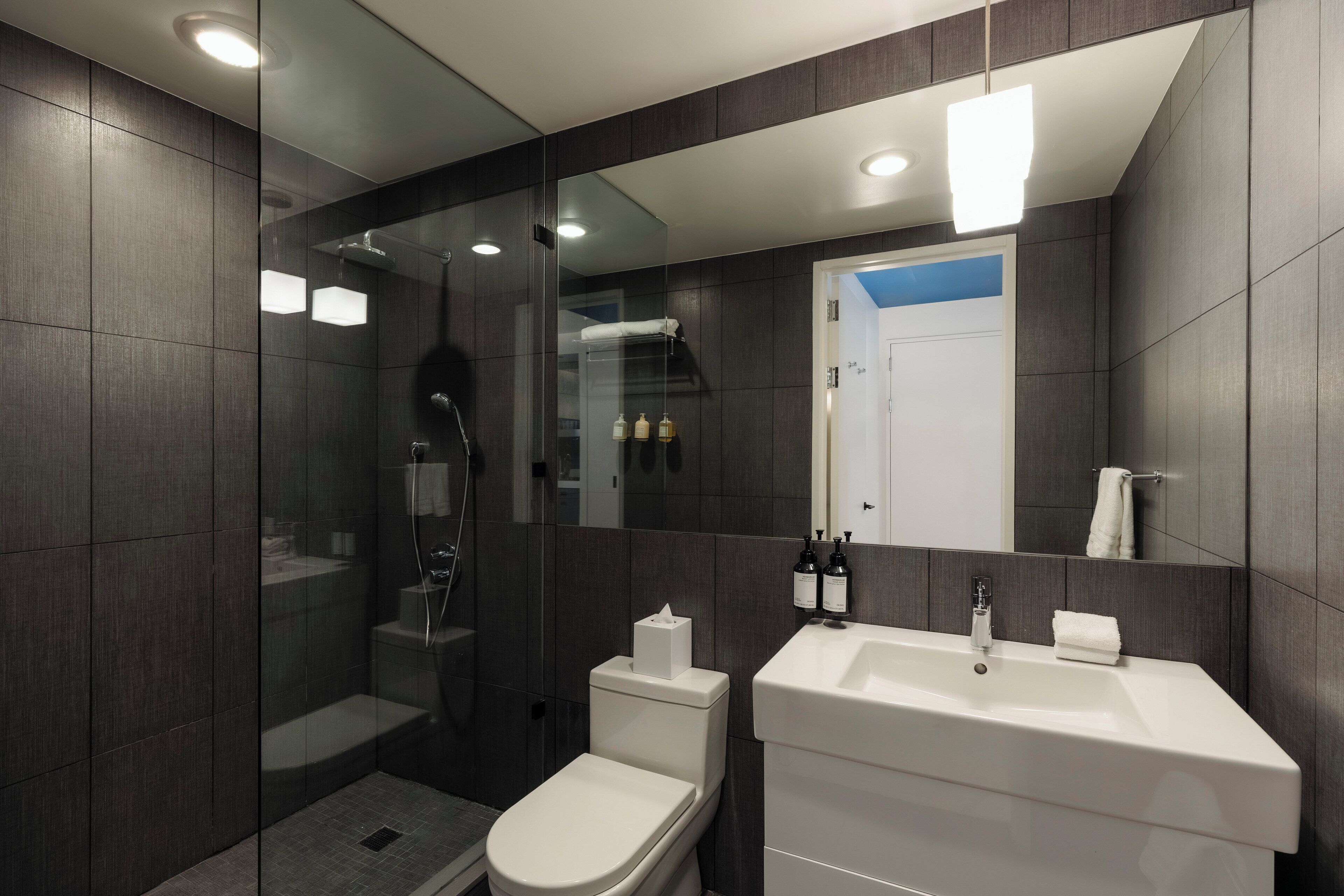 A modern bathroom with a glass-enclosed shower, a white toilet, and a large sink with a mirror above it.