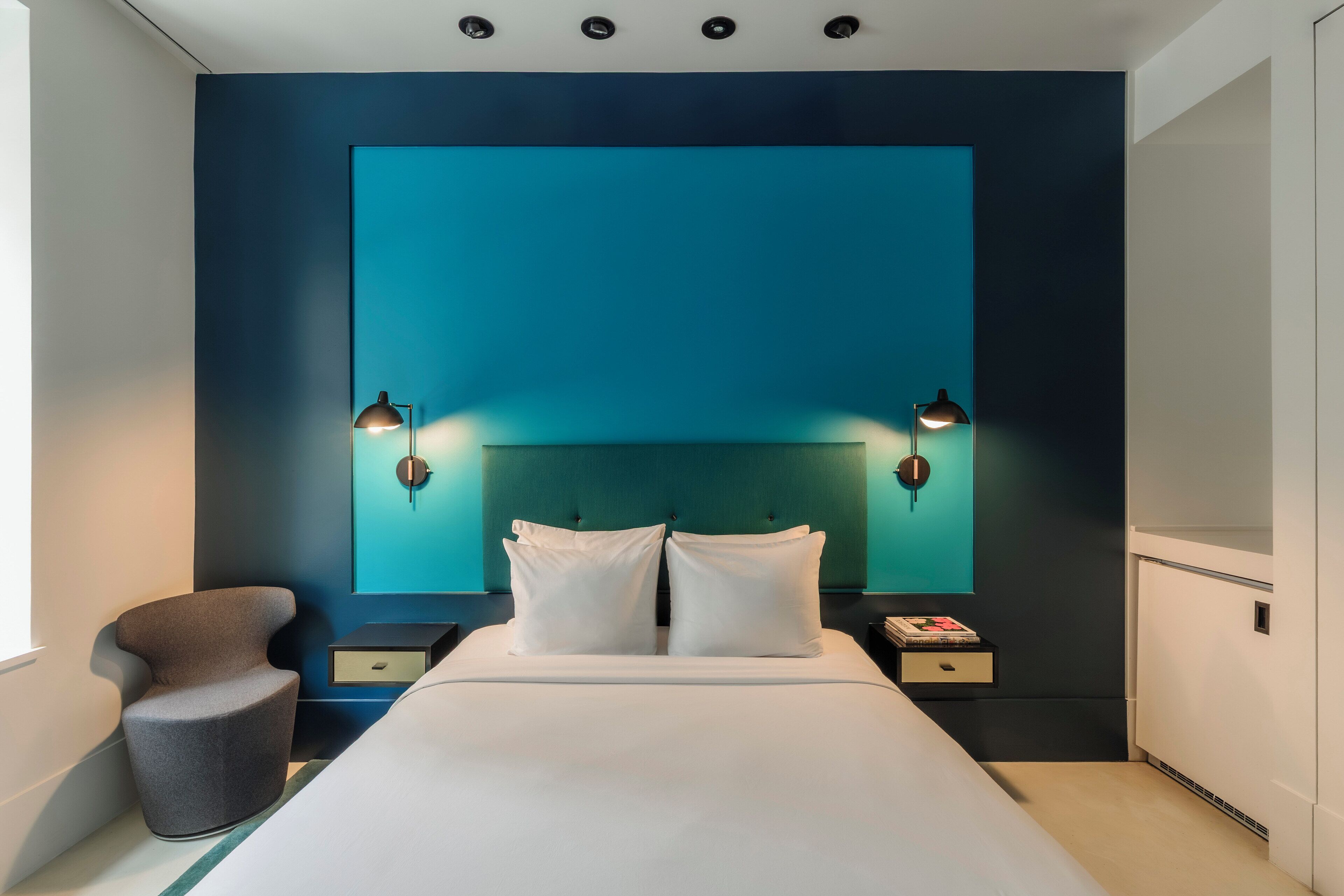A modern hotel room with a large bed, two bedside tables, a chair, and a wall-mounted TV.