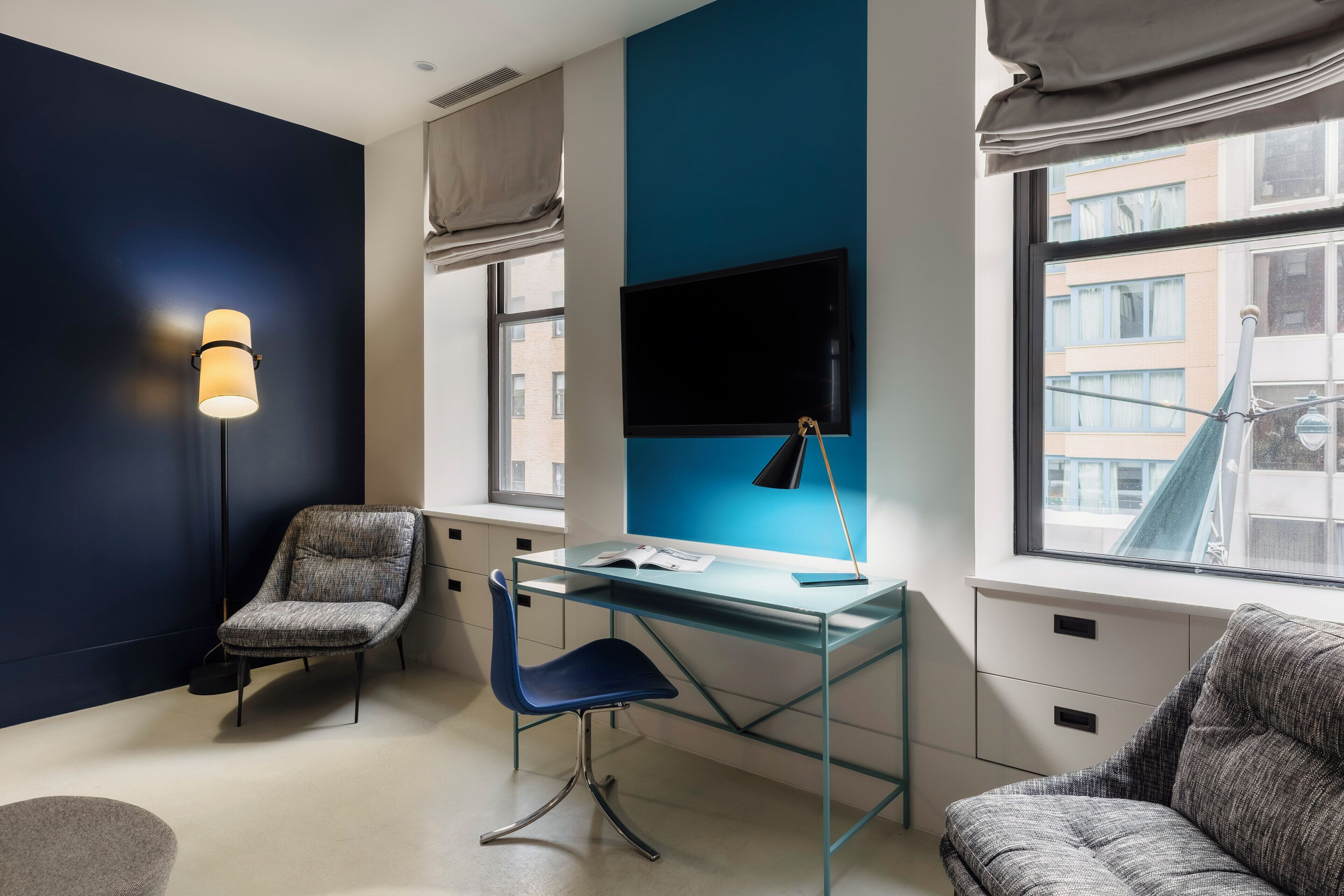 Una habitación moderna con un escritorio de vidrio, un muro azul decorativo, una televisión y vistas de edificios.