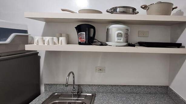 Eine Küche mit Spüle aus Edelstahl, einer Kaffeemaschine und einem Reiskocher auf der Arbeitsplatte.