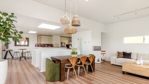 A modern living room with a wooden dining table, green upholstered chairs, a sofa, and a TV stand.