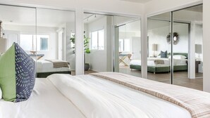 A modern bedroom with a large bed, a green pillow, and a view through a glass door to another room.
