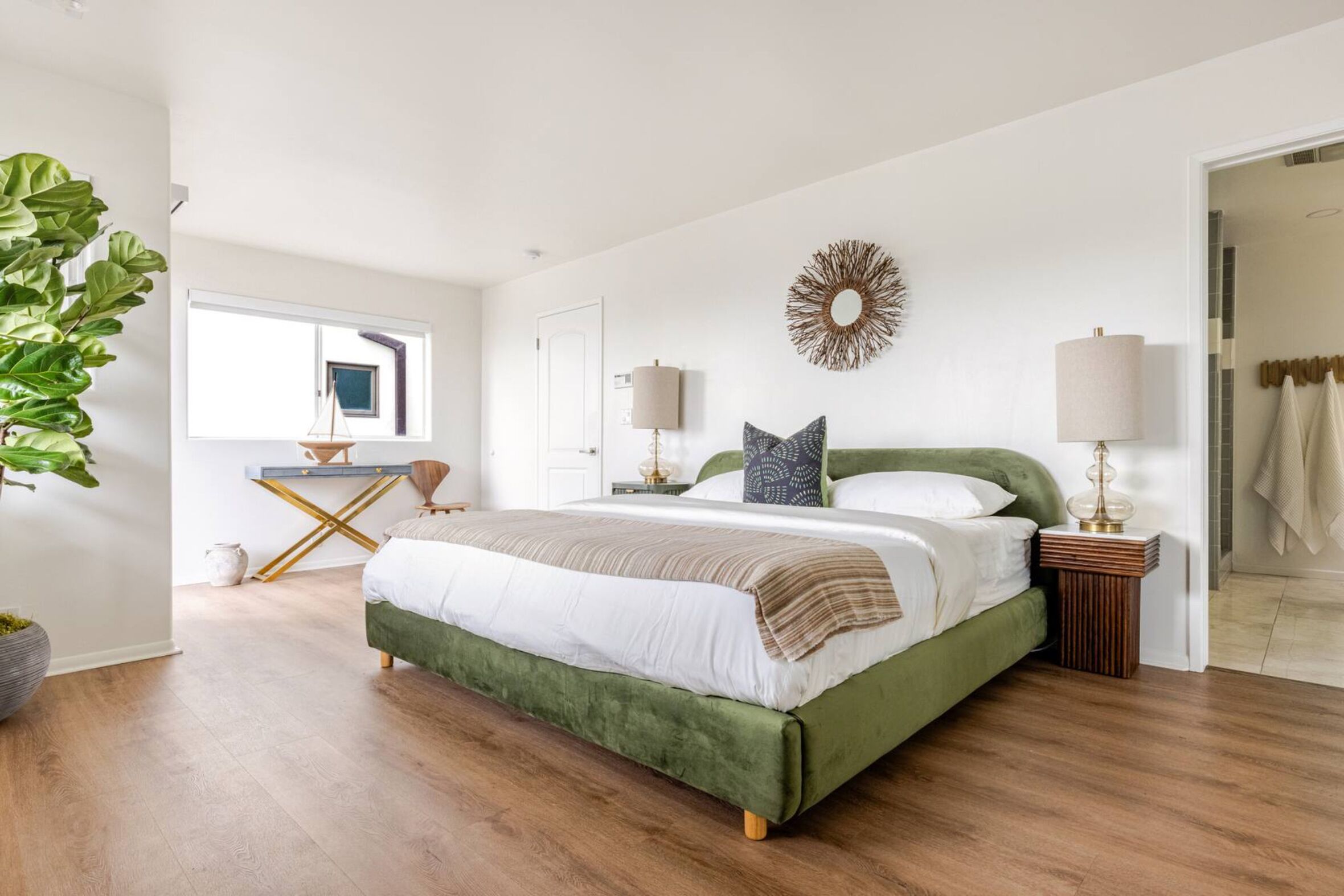 A bedroom with a large bed, a bedside table, a lamp, a wall decoration, and a potted plant.
