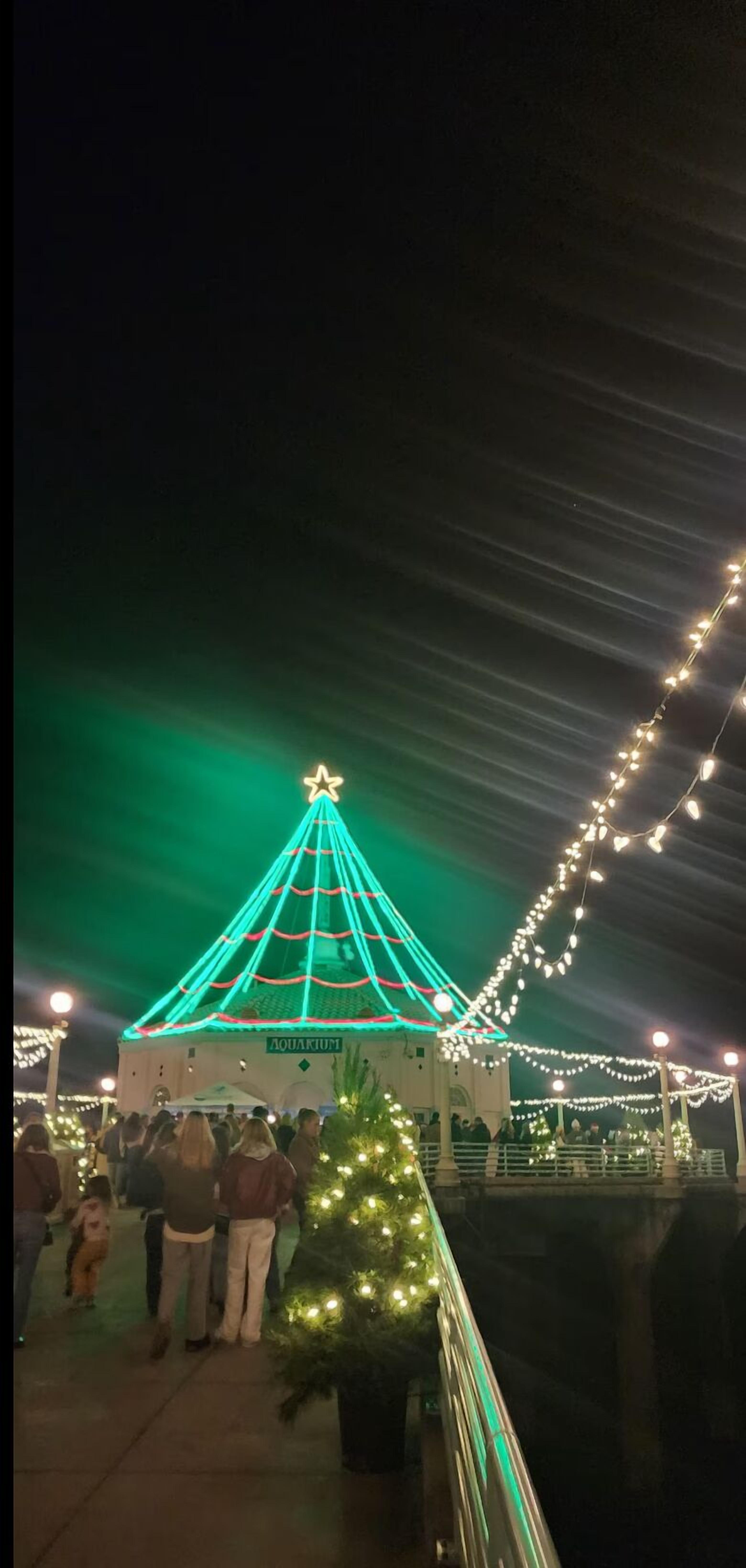 A building with a star on top, surrounded by string lights and a small Christmas tree.