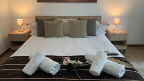 A neatly made bed with a white duvet, two bedside lamps, and a painting of a sunset over the ocean. - B&B Hideaway Haven Villa (Sant'Anna Arresi)
