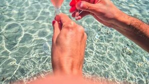 Two hands holding wine glasses with a clear blue sea and a hilly landscape in the background. - B&B Hideaway Haven Villa (Sant'Anna Arresi)