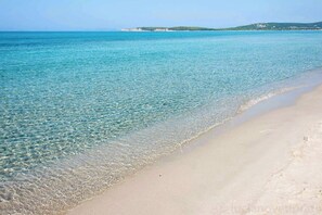 Una playa con aguas transparentes y poco profundas, y una orilla arenosa.