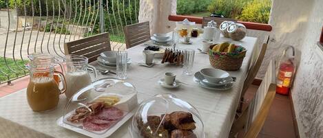 A breakfast table set outdoors with various food items, including pastries, bread, and condiments.
