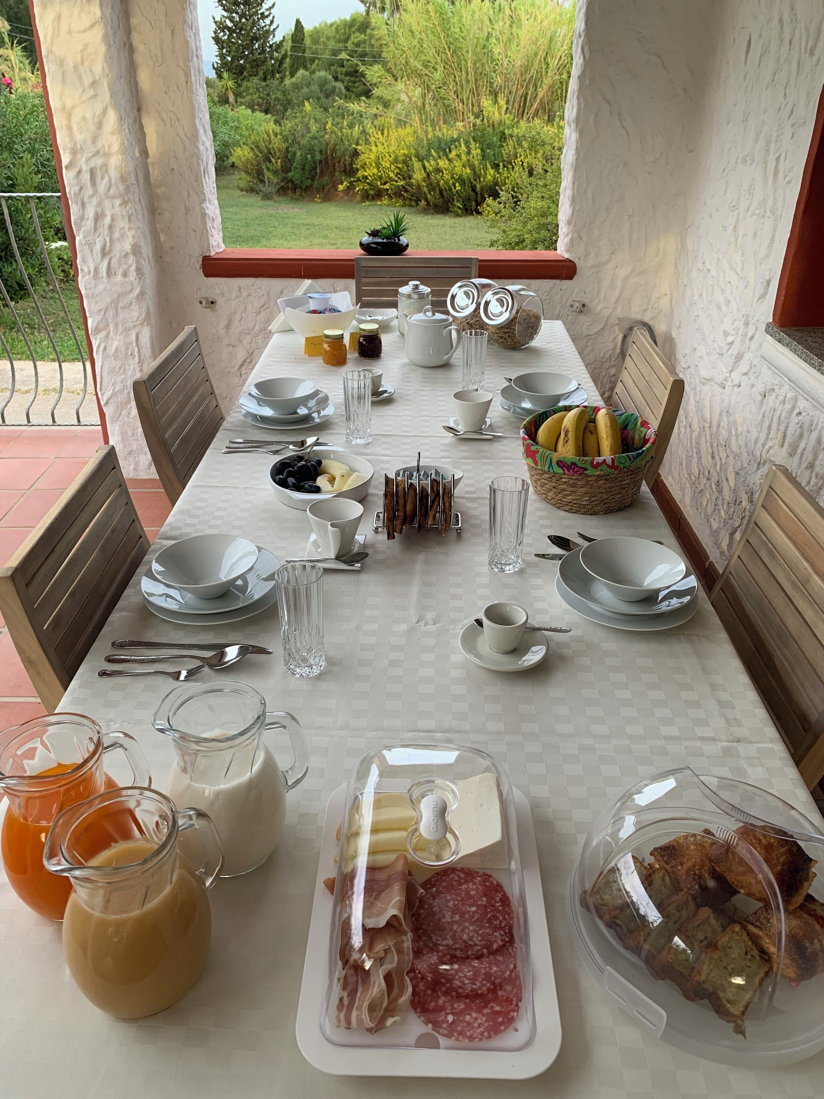 A table set for breakfast with various food items and drinks, overlooking a garden.