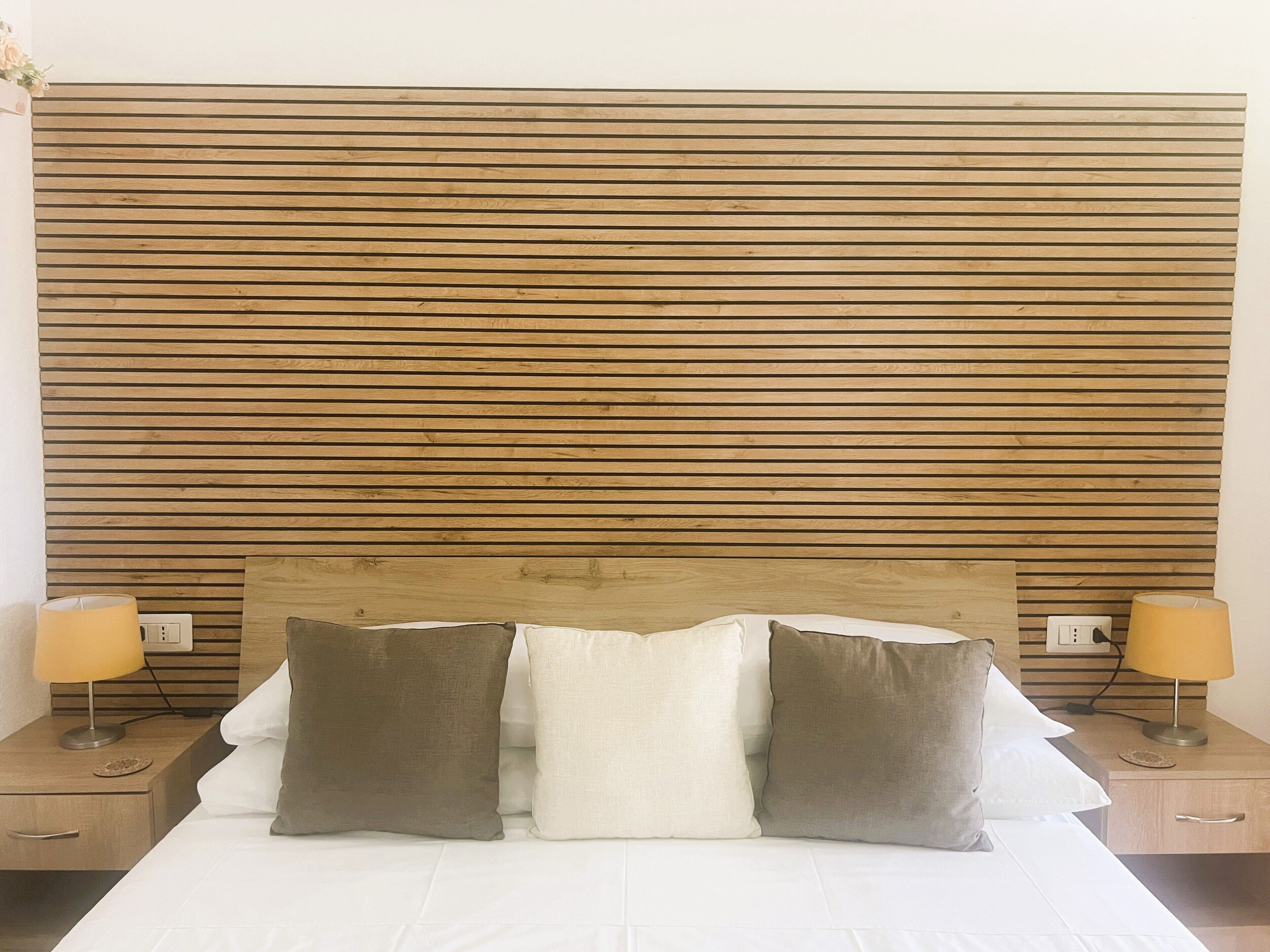 Una cama con cabecera de madera, dos mesitas de noche con lámparas y una colcha blanca.