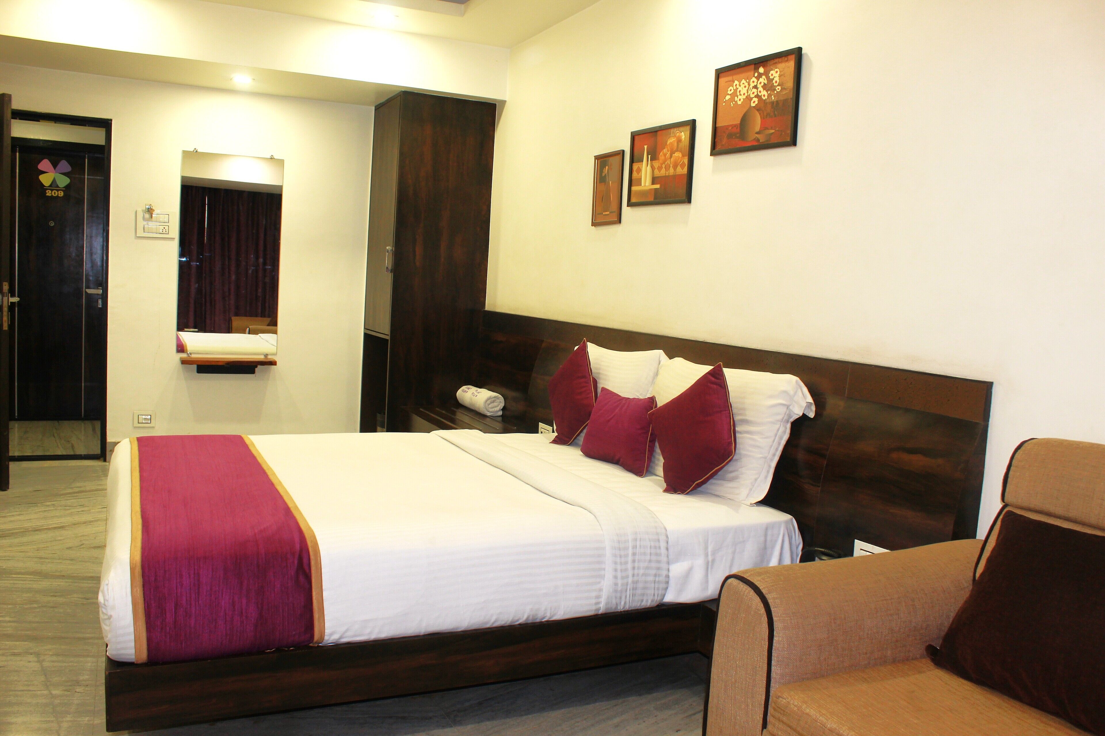 A hotel room with a large bed, a wooden headboard, a brown armchair, and a mirror on the wall.