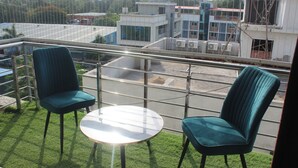 A balcony with two chairs and a small table, overlooking a street with buildings and a clear sky. - Hotel Planet Four (Mawal)