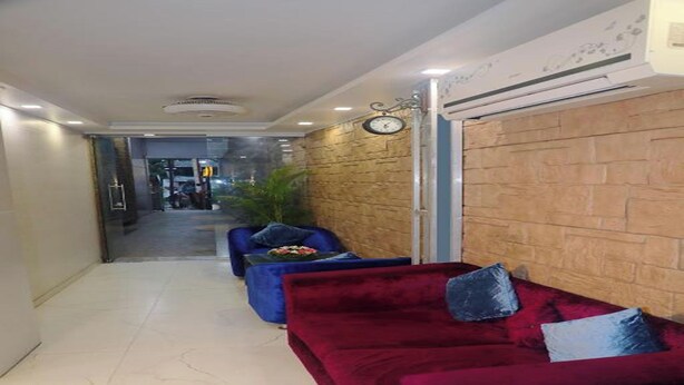 A hallway with a red sofa and a blue sofa, a clock on the wall, and a wooden accent wall. - Hotel Planet Four (Mawal)