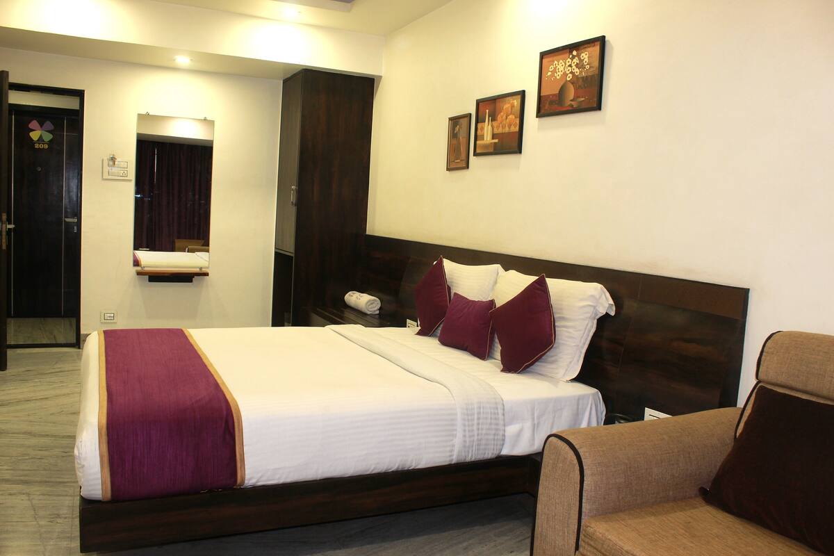 A hotel room with a large bed, a wooden headboard, a chair, and a mirror.