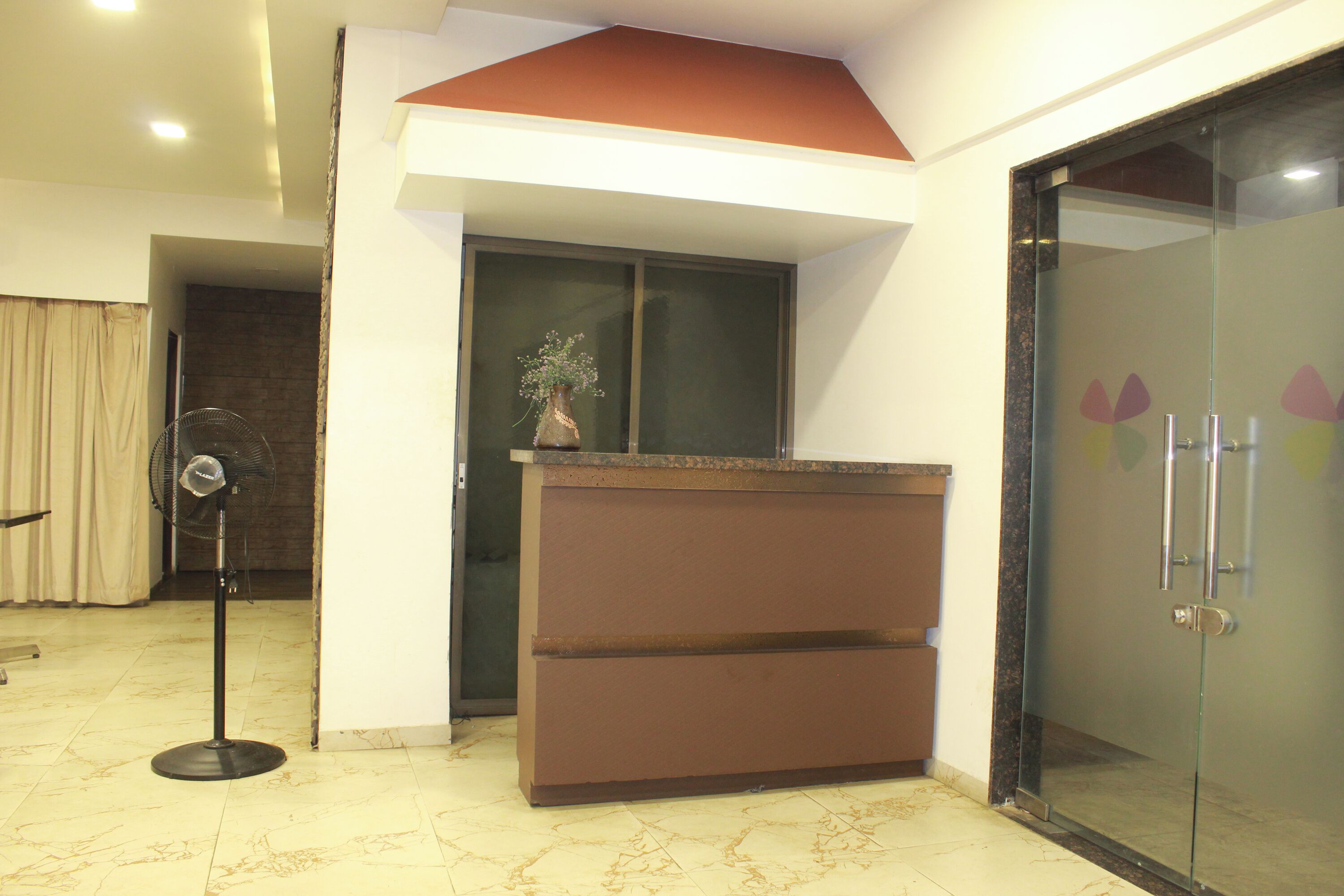 A reception area with a marble floor, a brown reception desk, a glass door with a frosted pattern, and a standing fan.