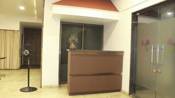 A reception area with a marble floor, a brown reception desk, a glass door with a frosted pattern, and a standing fan.
