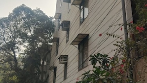 A multi-story building with balconies, a parked car, and surrounding greenery.