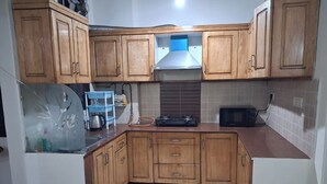 A kitchen with wooden cabinets, a stainless steel range hood, a microwave, and a kettle on the countertop.