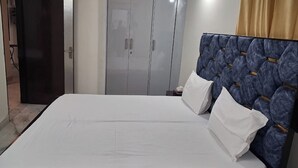 A bed with a white mattress and two pillows, a blue headboard, and a wardrobe with silver handles.
