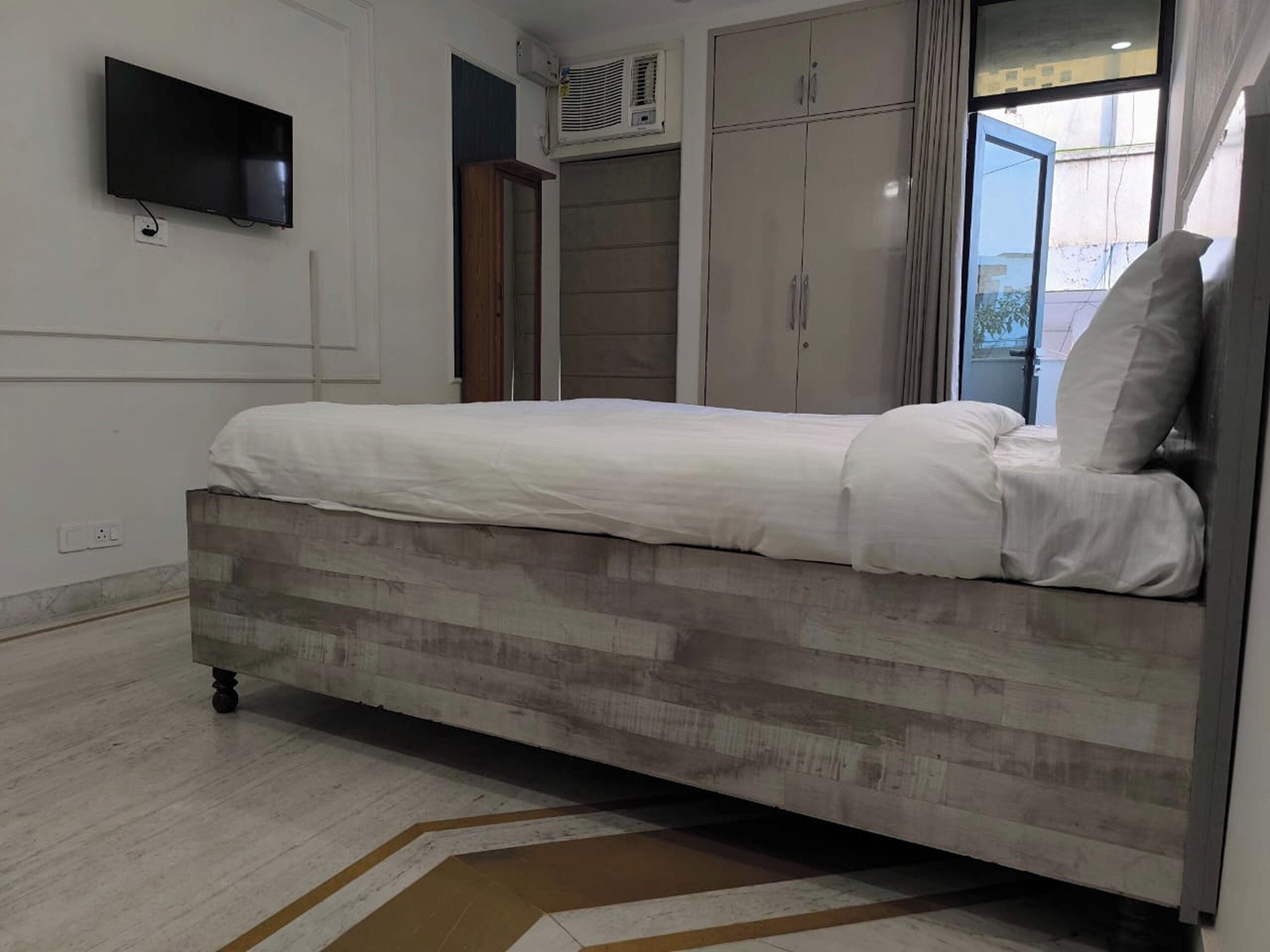 A bedroom with a bed, a TV mounted on the wall, and a wardrobe.