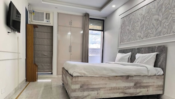 Un dormitorio con cama, armario, televisor y ventana con cortinas.