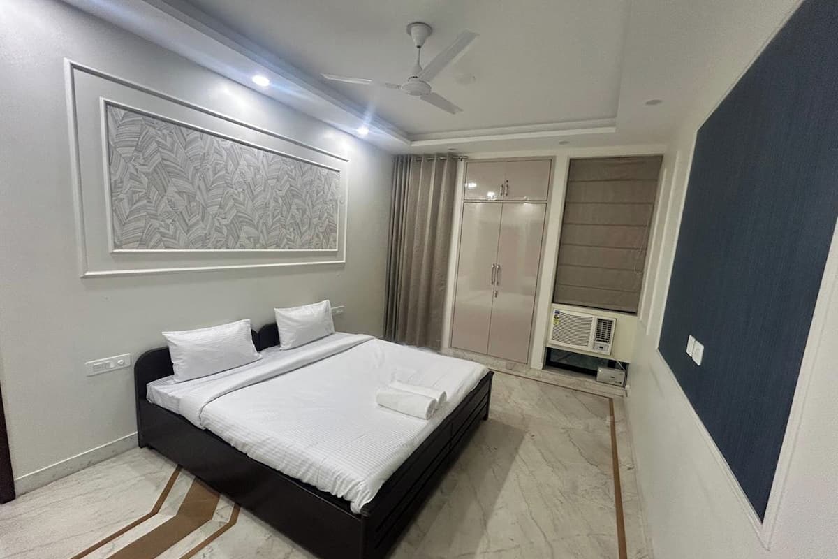 Un dormitorio con cama, ventilador de techo, armario y un amplio ventanal con cortinas.