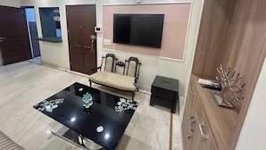 Un salón amplio con una mesa de centro de vidrio negro, un sofá, un televisor montado en la pared y un mueble de madera.