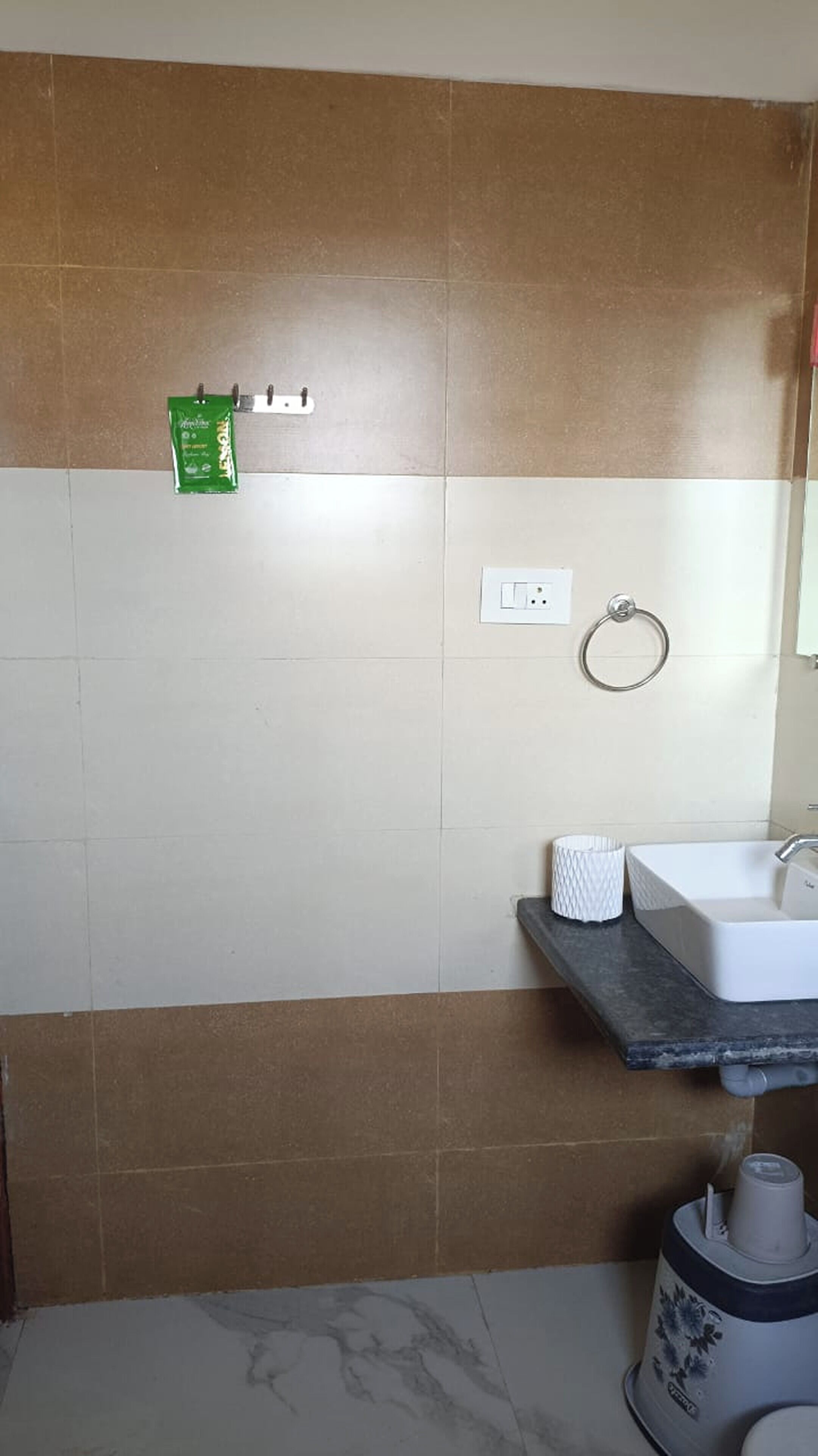 Un baño con un lavamanos blanco, un tocaderechas para toallas y un paquete verde en la pared.