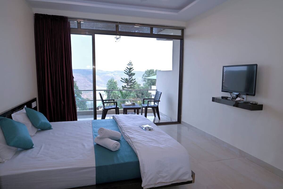 Ein Hotelzimmer mit einem großen Bett, einem an der Wand montierten Fernseher und einem Balkon mit Tisch und Stühlen.