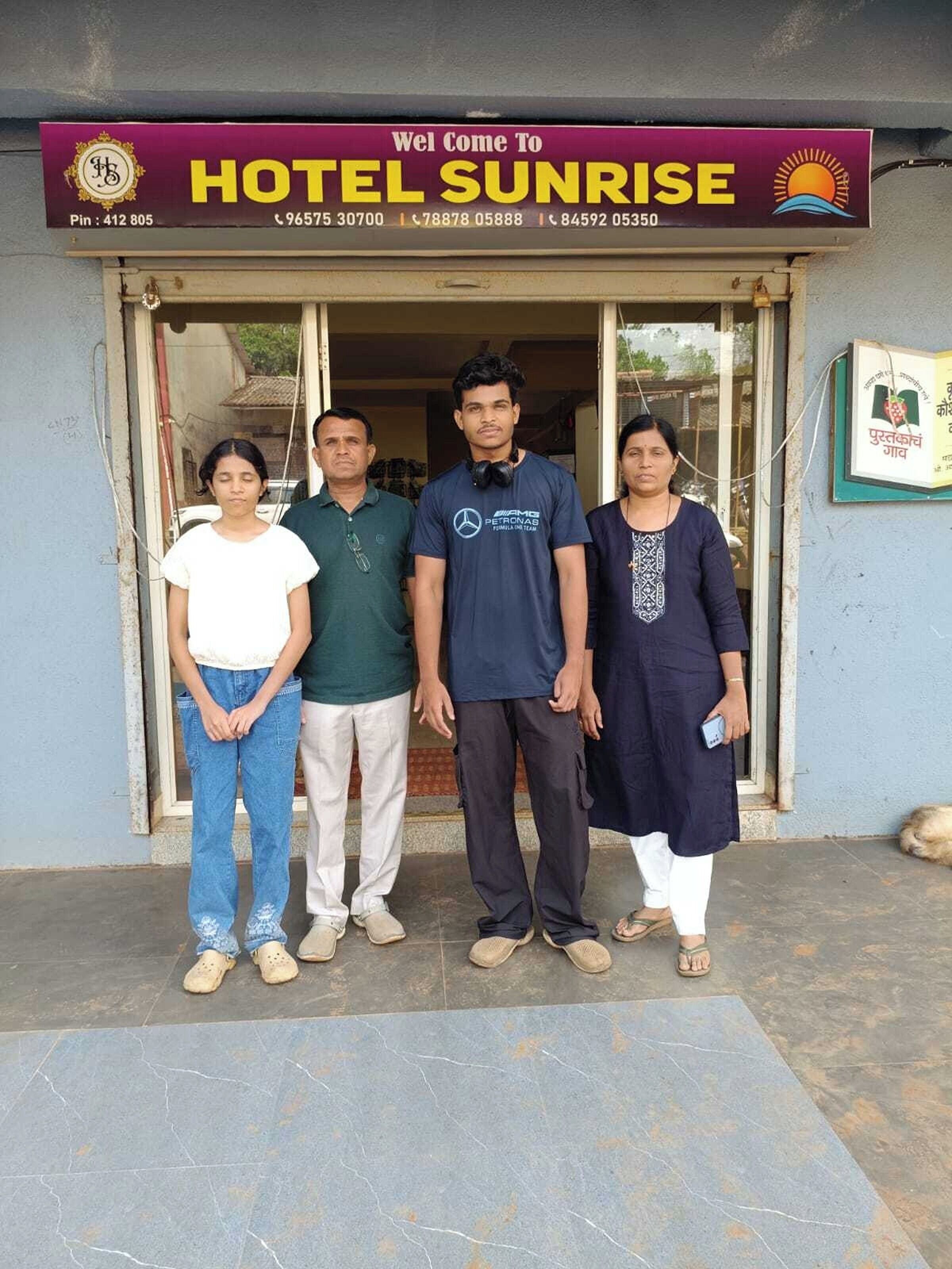 Une famille se tient devant un hôtel appelé «HÔTEL SUNRISE», dont les numéros de téléphone sont clairement affichés.